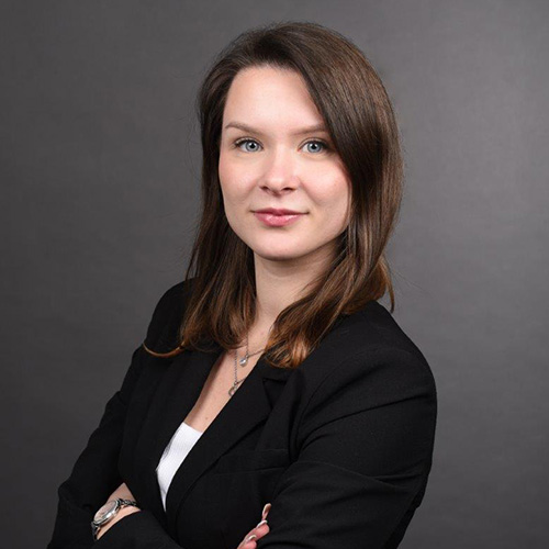 expertum - Fachkraft in Business-Kleidung mit verschränkten Armen vor grauem Hintergrund, symbolisiert Karriere und Zusammenarbeit in der Industrie.