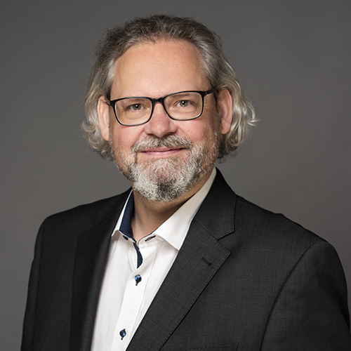 expertum - Ein freundlicher, erfahrener Mann im Anzug vor neutralem Hintergrund - Sinnbild für Fachkräftevermittlung und industrielle Zusammenarbeit.