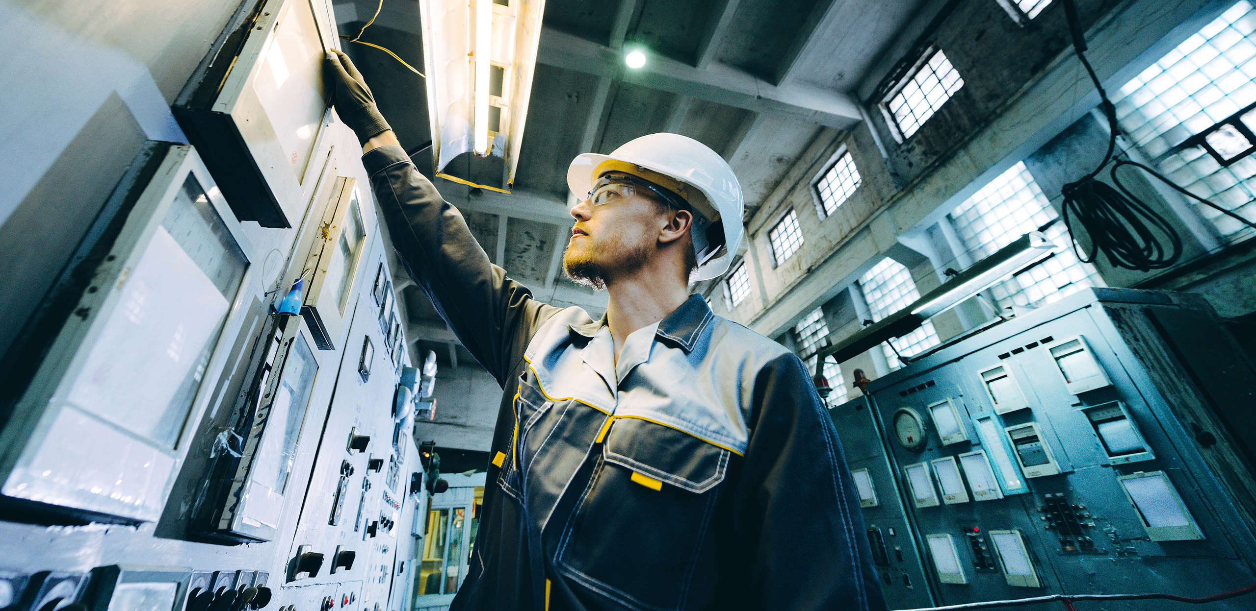 expertum - Eine Fachkraft mit Schutzhelm und Schutzbrille bedient Steuerpulte in einer Industrieanlage, umgeben von Maschinen und Beleuchtung. Das Bild zeigt typische Arbeitsumgebungen in der Industrie und veranschaulicht den Zusammenhang zwischen technischem Know-how und sicherheitsbewusstem Arbeiten – zentrale Aspekte für Bewerberinnen und Bewerber sowie für Unternehmen in den Bereichen Personalvermittlung, moderne Projektarbeit und Fachkräftebedarf.
