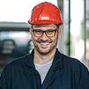 expertum - Eine Person mit Brille, rotem Schutzhelm und dunkler Jacke steht in einem Innenraum, der an eine industrielle oder bauliche Umgebung erinnert. Das Bild vermittelt den Eindruck von beruflicher Einsatzbereitschaft in der Industrie und kann sowohl Bewerber*innen als auch Unternehmen im Zusammenhang mit Personalvermittlung, Fachkräftesuche oder projektbezogener Zusammenarbeit ansprechen.