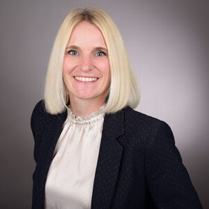 expertum - Eine Frau mit schulterlangem, blondem Haar in Businesskleidung, vor neutralem Hintergrund - Symbolbild für Personalvermittlung in der Industrie.