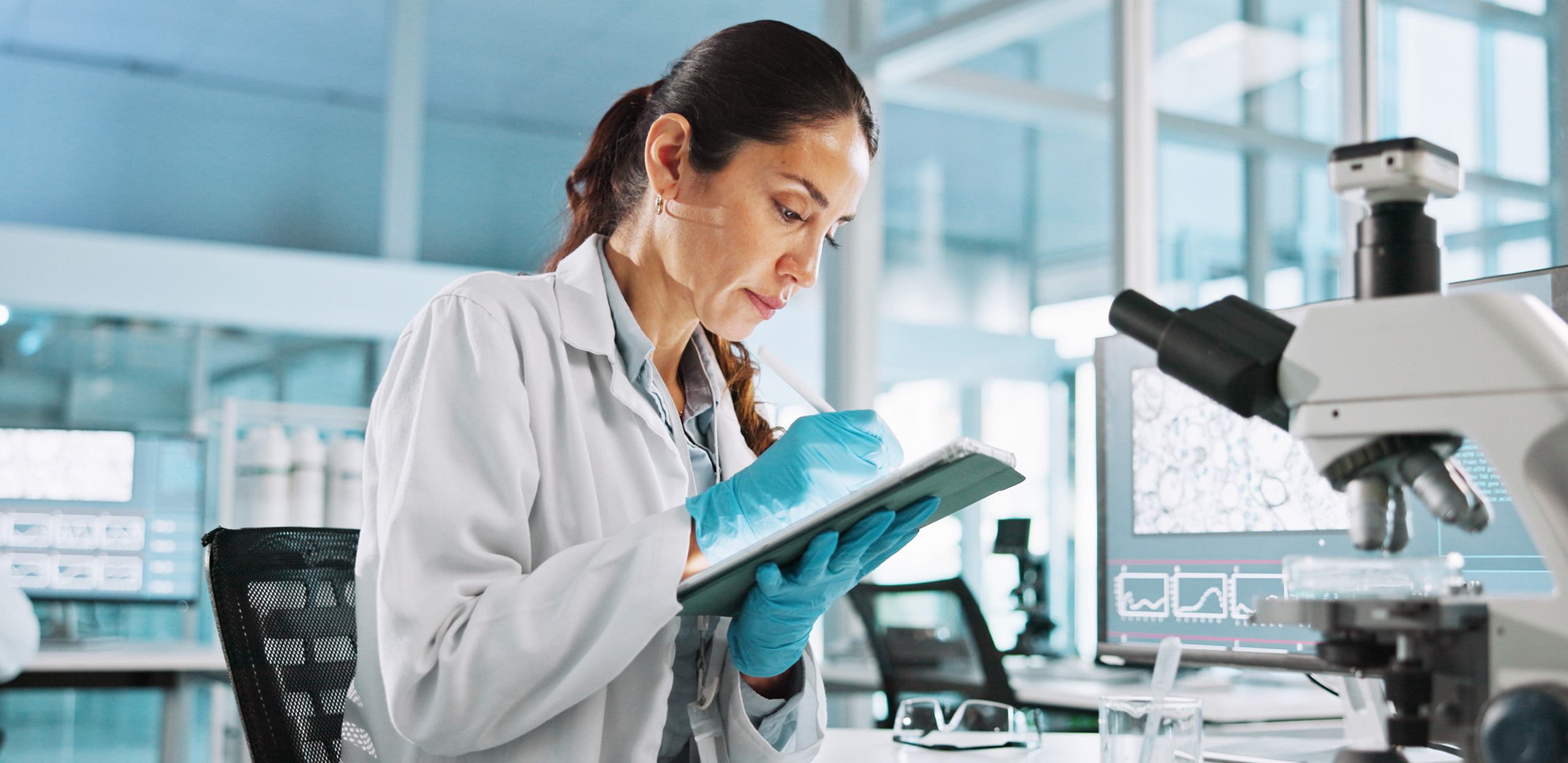 expertum - Ein Wissenschaftler in Laborkittel und Handschuhen tippt konzentriert auf einem Tablet in einem modernen Labor. Im Hintergrund sind ein Mikroskop sowie mehrere Bildschirme mit wissenschaftlichen Daten zu sehen. Die Szene verdeutlicht die Bedeutung von Fachkräften im Bereich Forschung und Entwicklung sowie das Zusammenspiel moderner Technologien im industriellen Arbeitsumfeld – relevante Aspekte sowohl für Unternehmen auf der Suche nach Personal als auch für Bewerber, die sich für Projektarbeit oder Karrieremöglichkeiten in der Industrie interessieren.