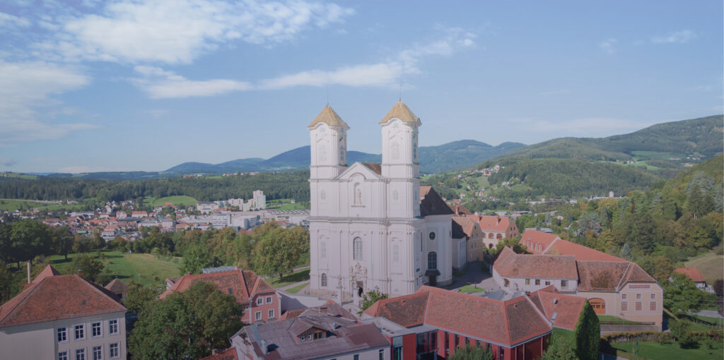 expertum - Eine weiße Kirche mit Türmen in einer Kleinstadt, geprägt von Personaldienstleistung im industriellen Umfeld, umgeben von Natur in Weiz (Österreich).