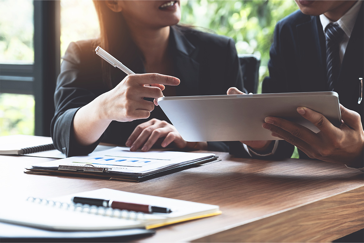 expertum - Zwei Personen in Businesskleidung sitzen an einem Schreibtisch und schauen gemeinsam auf ein Tablet. Auf dem Tisch liegen Diagramme, Notizbücher und Stifte. Beide wirken konzentriert, während sie über ein Stellenangebot sprechen, was den Austausch zwischen Fachkräften und Unternehmen in der industriellen Personalvermittlung sowie Themen wie Projektarbeit oder berufliche Weiterentwicklung widerspiegelt.